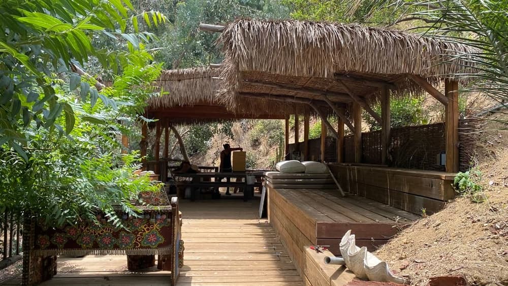 Rustic thatched-roof shelters on wooden deck surrounded by greenery people at tables